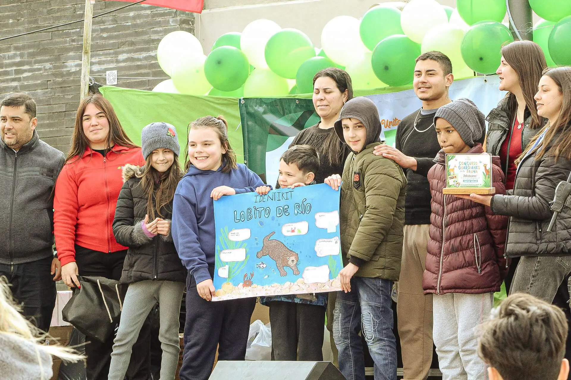 Niños y adultos posan en el escenario con un afiche escolar sobre el lobito de río.