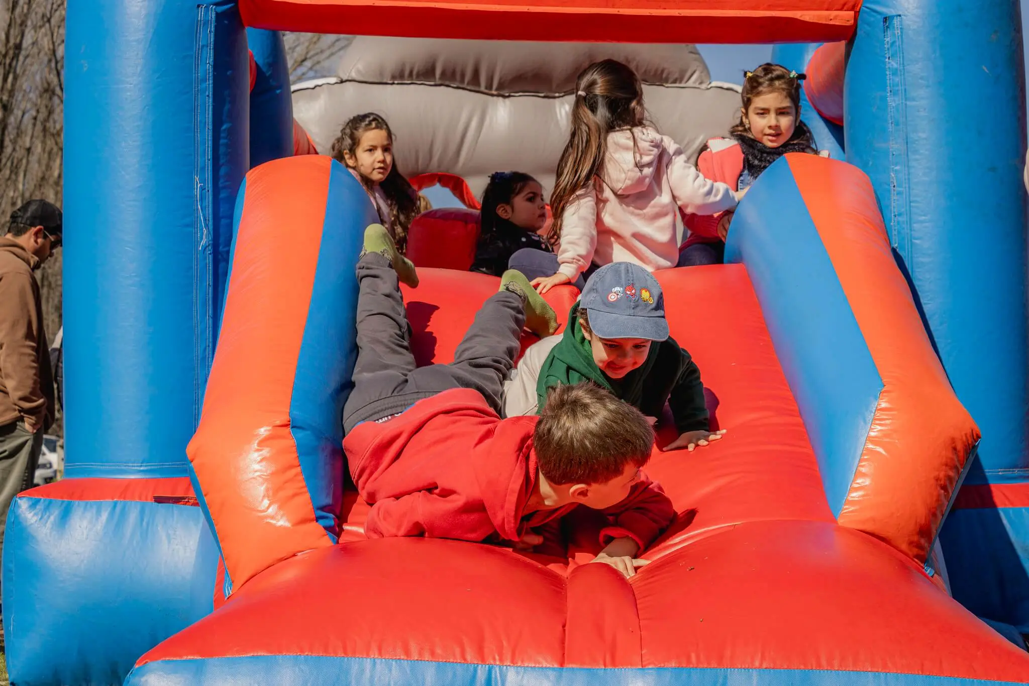 Niños se deslizan boca abajo por un tobogán inflable rojo y azul.