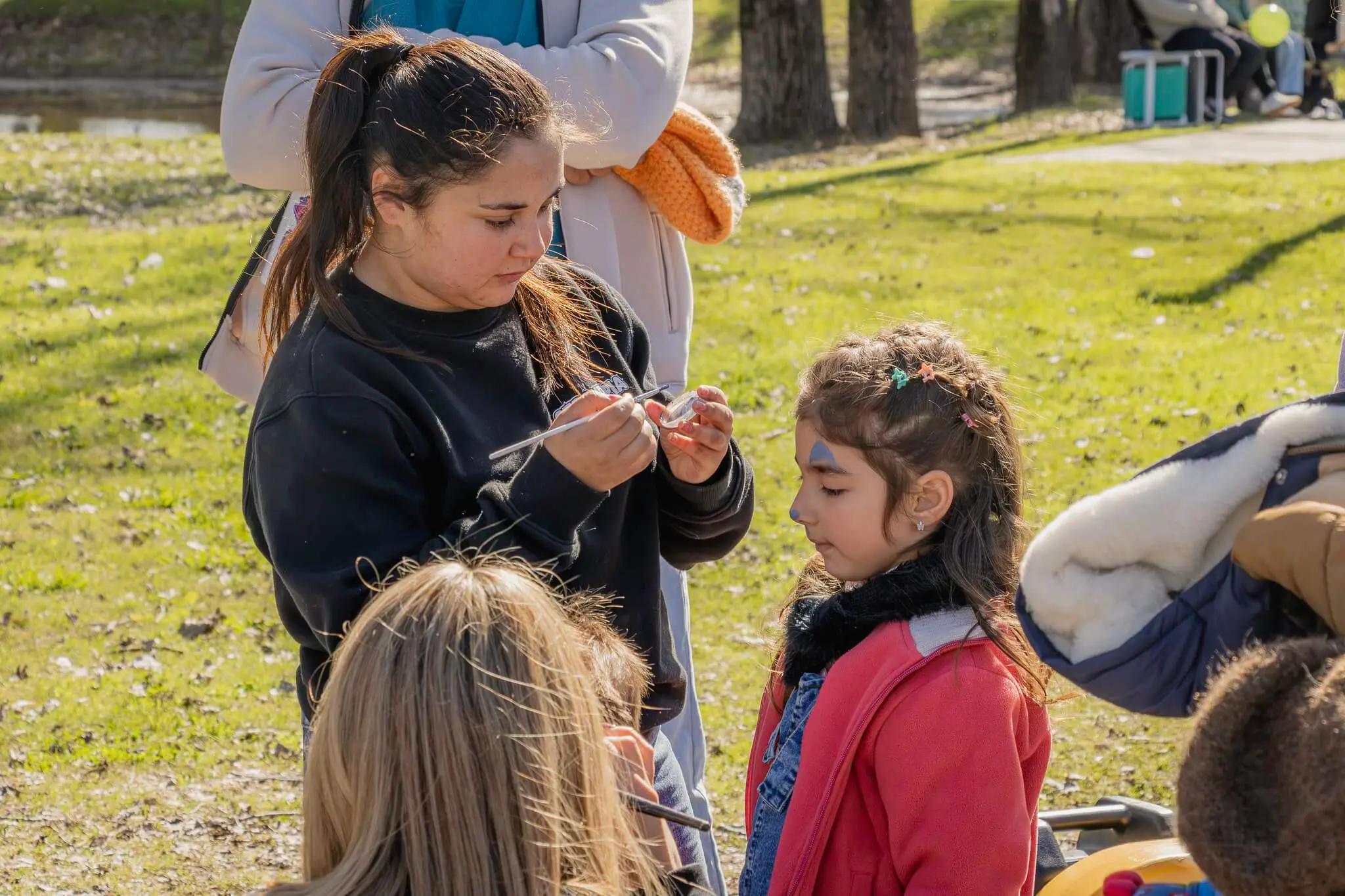 Una joven atiende a una niña con la cara pintada en un puesto del parque.