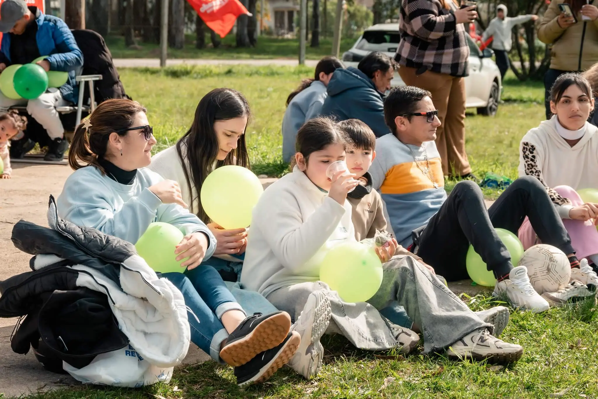 Familias sentadas en el césped con globos verdes, compartiendo la tarde.