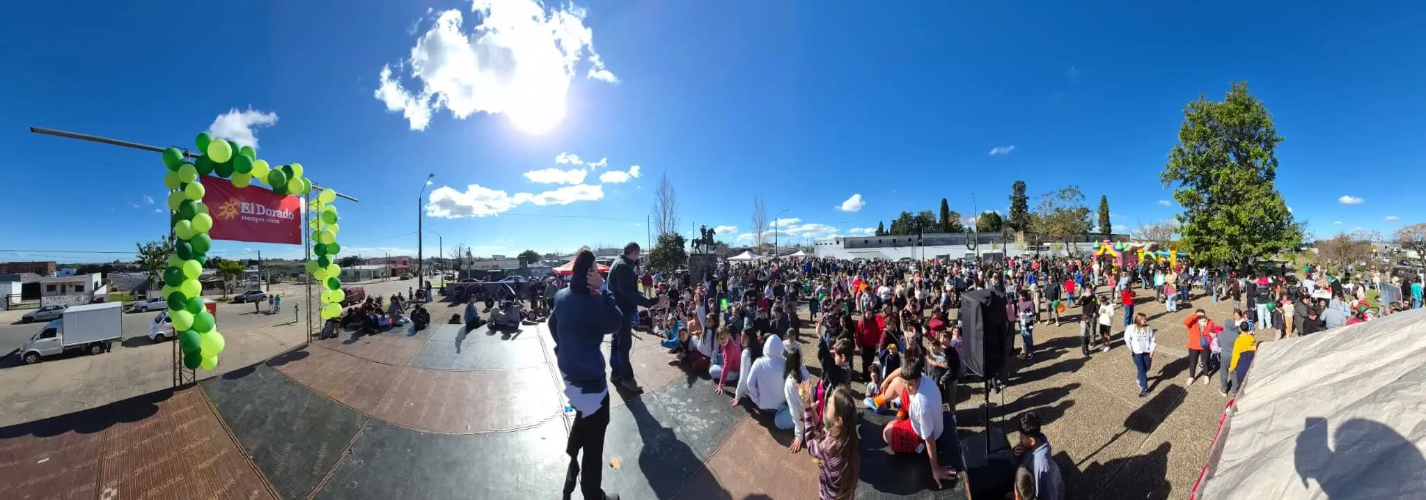 Panorámica de la plaza con arco de globos verdes y cientos de personas.