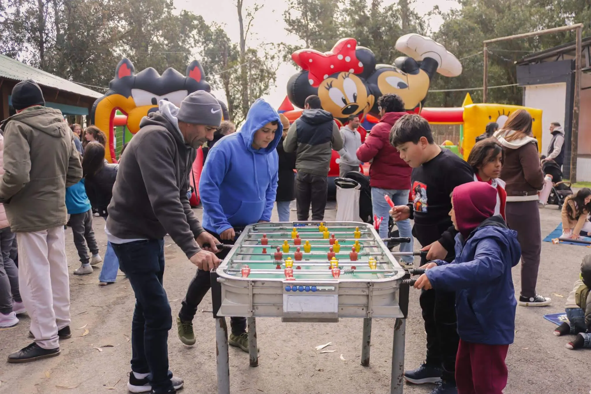 Adultos y niños juegan al futbolito, con personajes de Minnie y Mickey detrás.