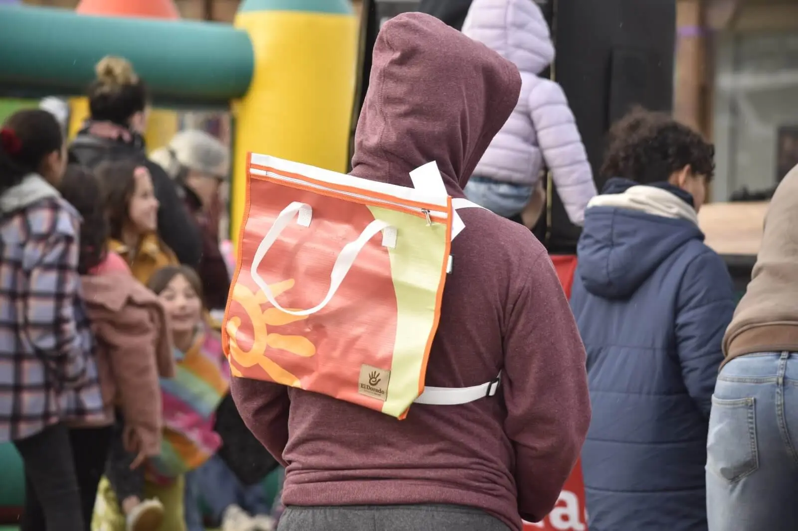 Una persona de espaldas lleva en la mochila una bolsa naranja de regalo de El Dorado.