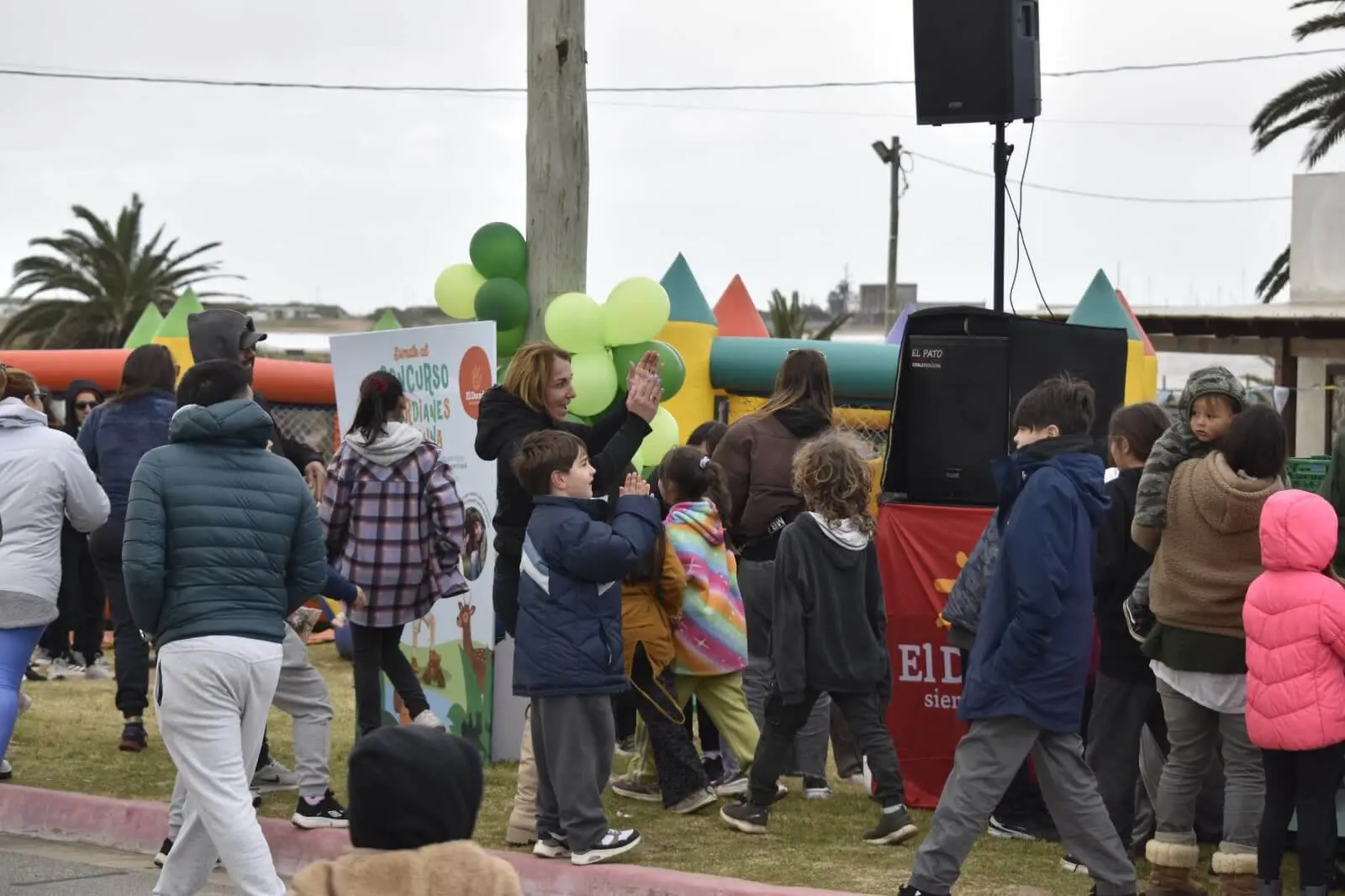 Niños y familias hacen fila entre inflables y un escenario con parlantes.