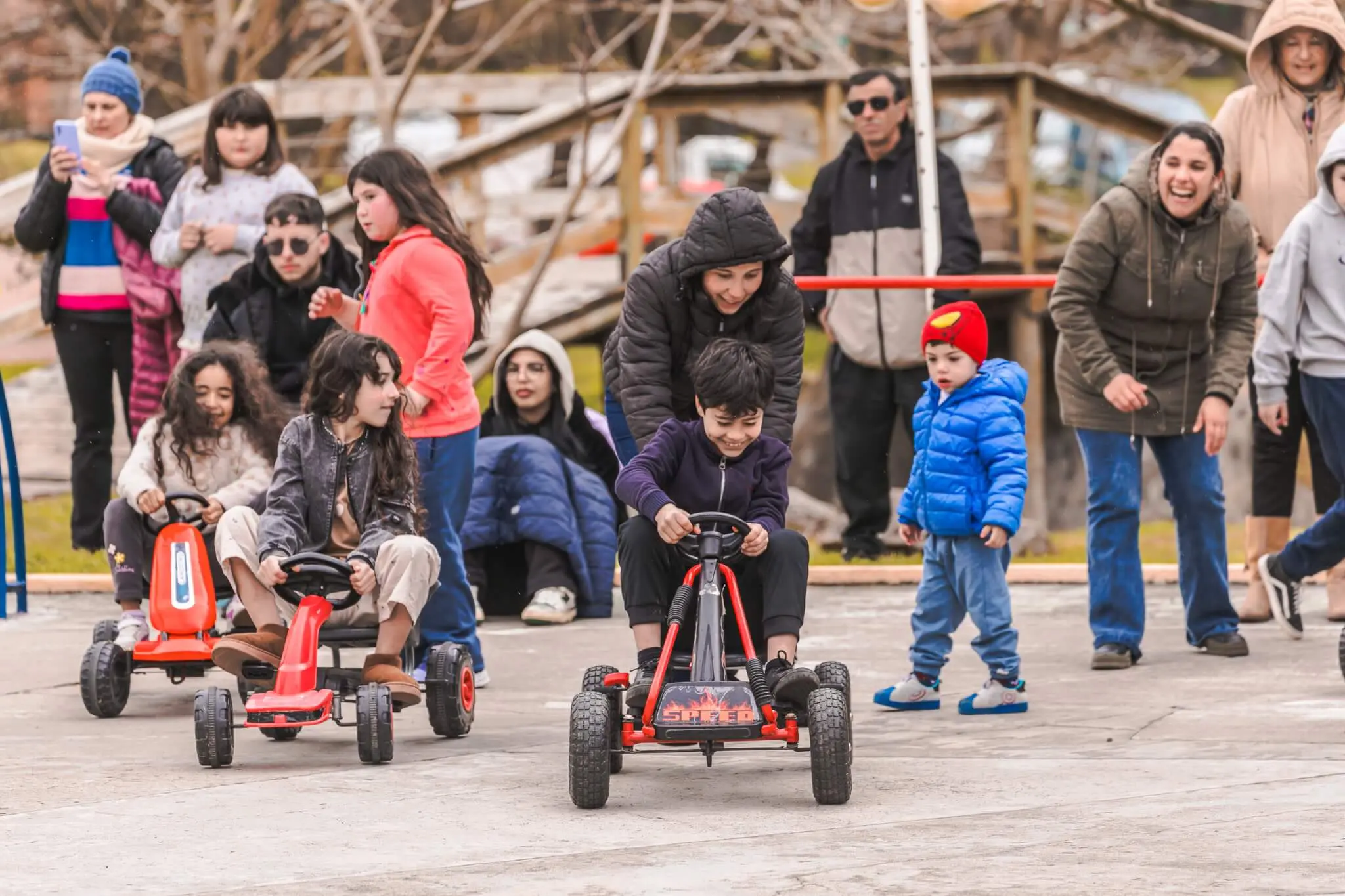 Niños corren carreras en autitos a pedal mientras las familias alientan.