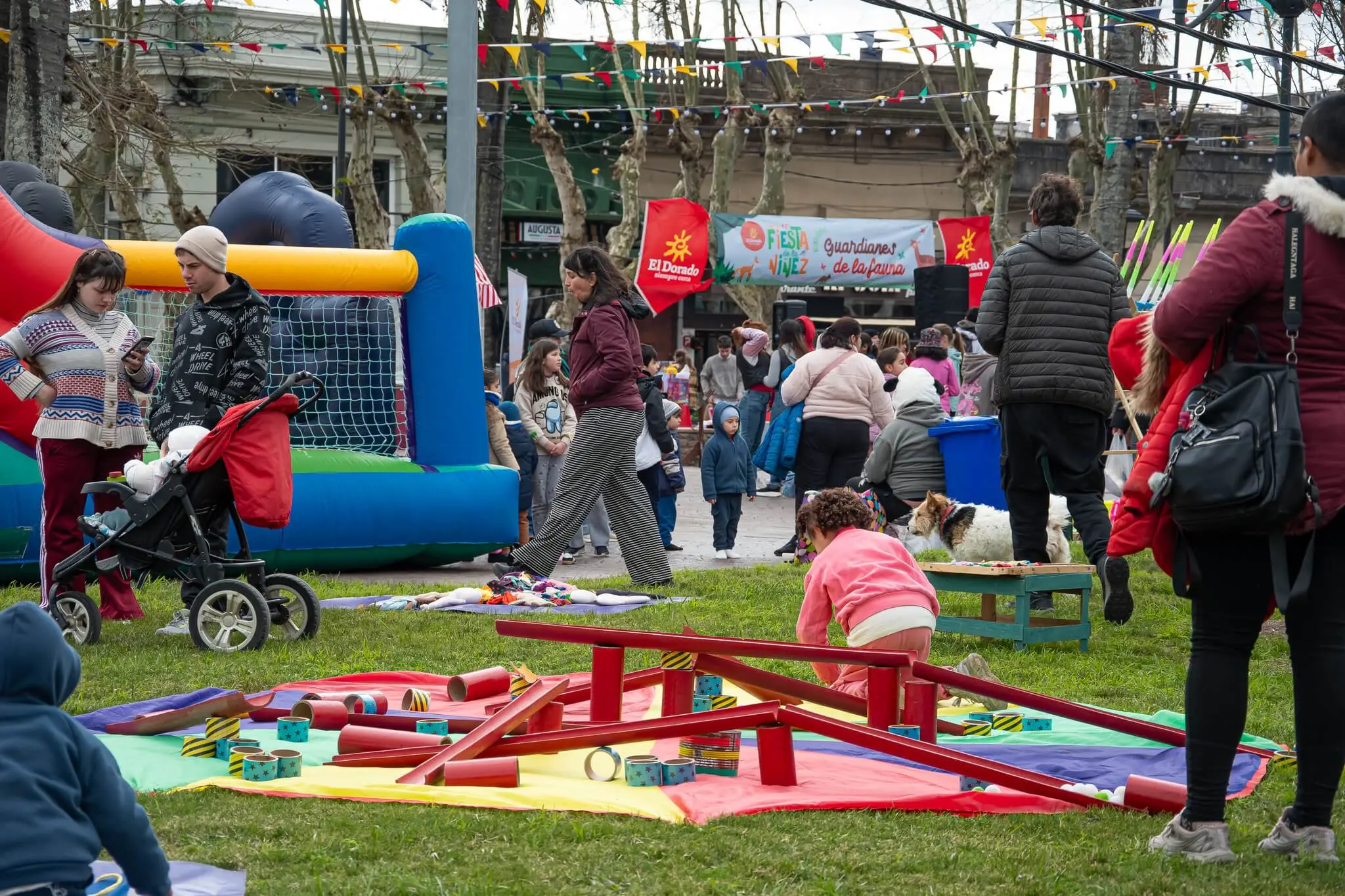 Niños juegan en un sube y baja y en inflables sobre el césped de la plaza.