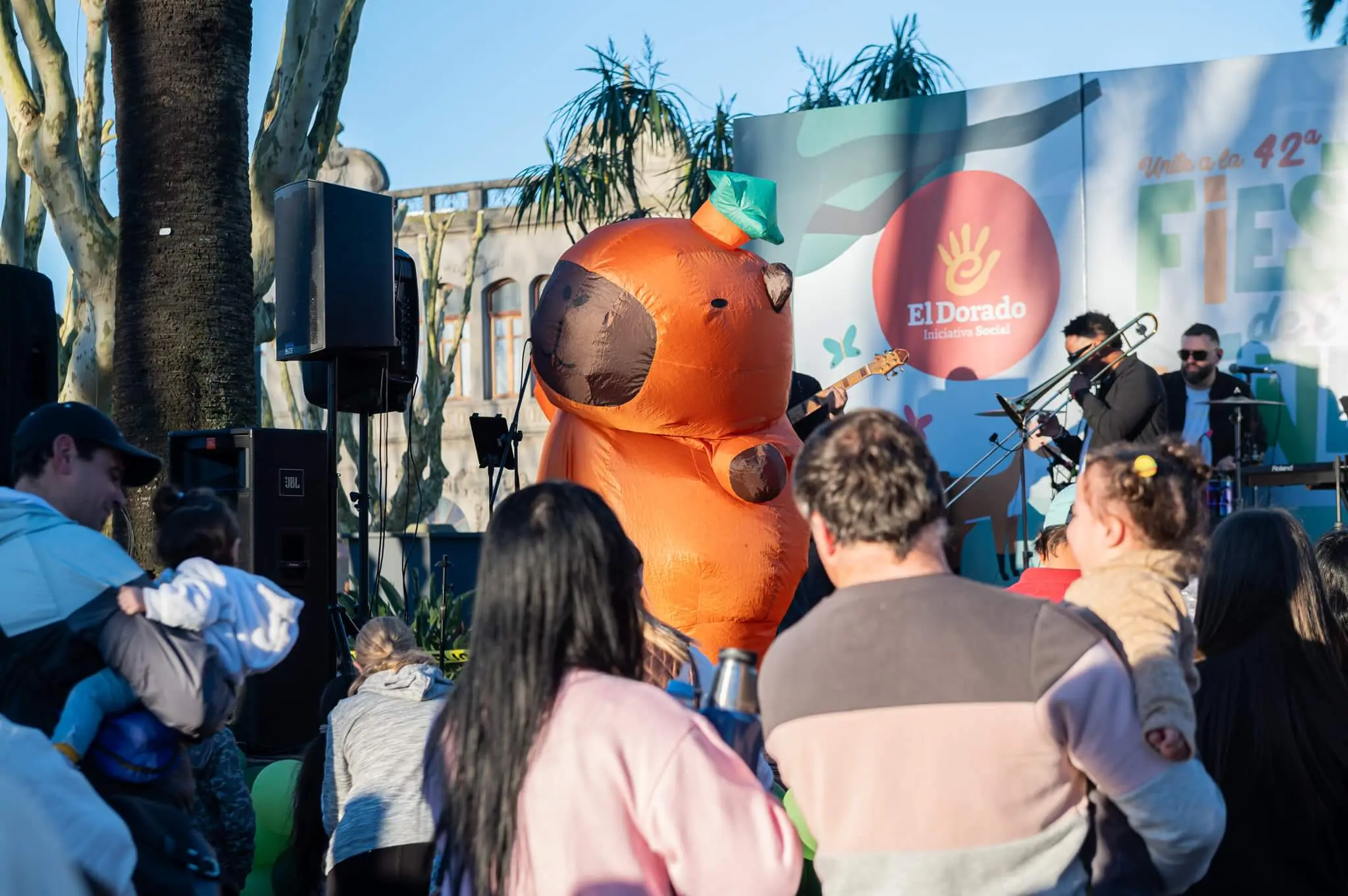 Una banda toca en el escenario de El Dorado junto a la capibara inflable mientras las familias miran.