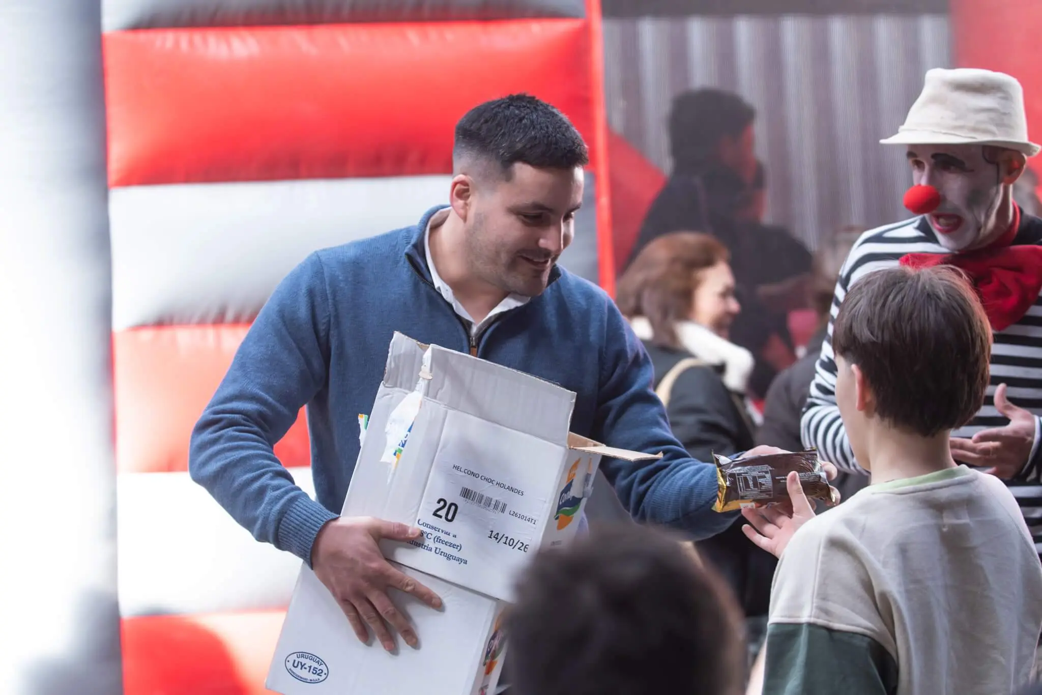 Un colaborador de El Dorado reparte regalos de una caja a los niños junto al payaso.