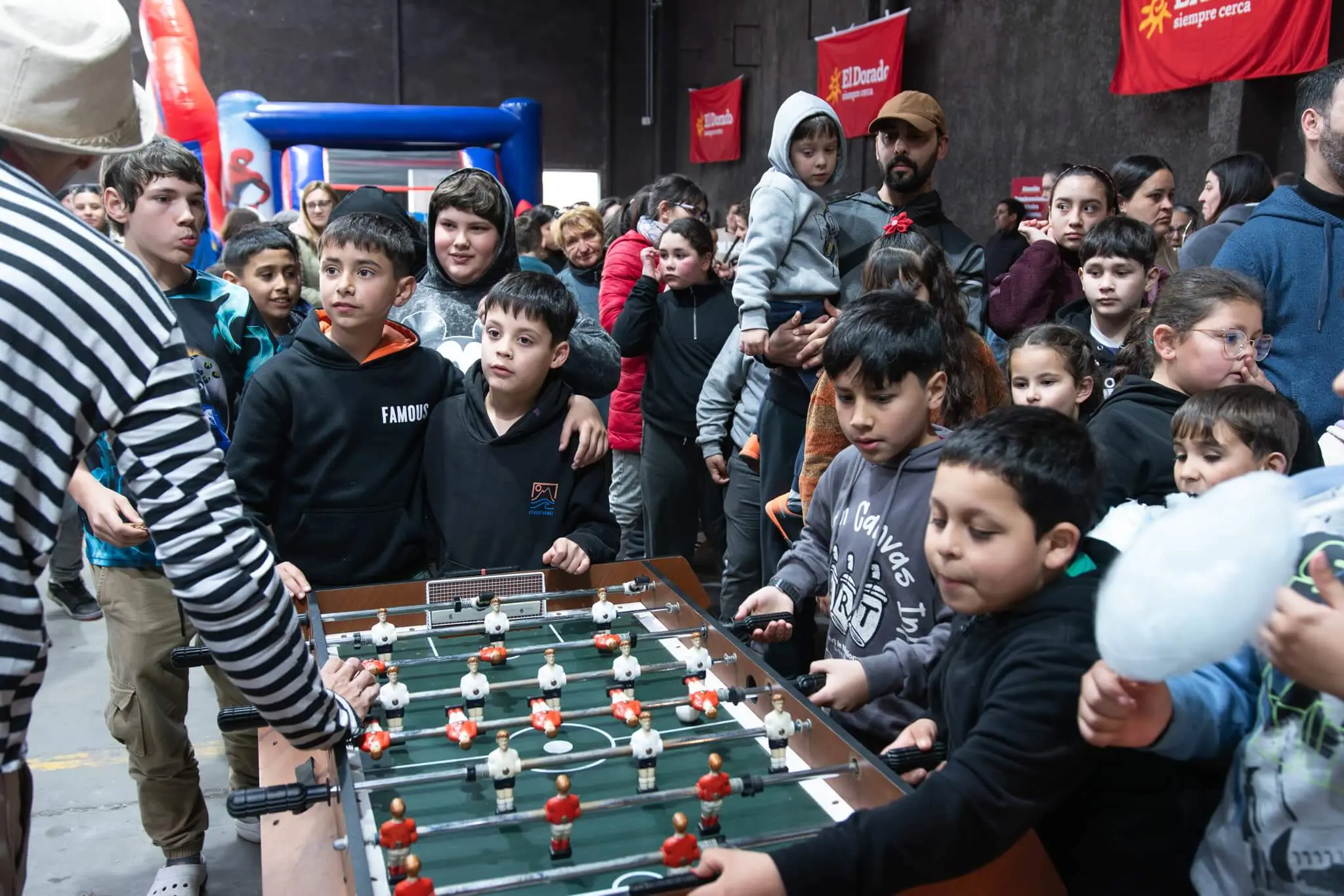 Niños juegan al futbolito rodeados de otros chicos que esperan su turno.