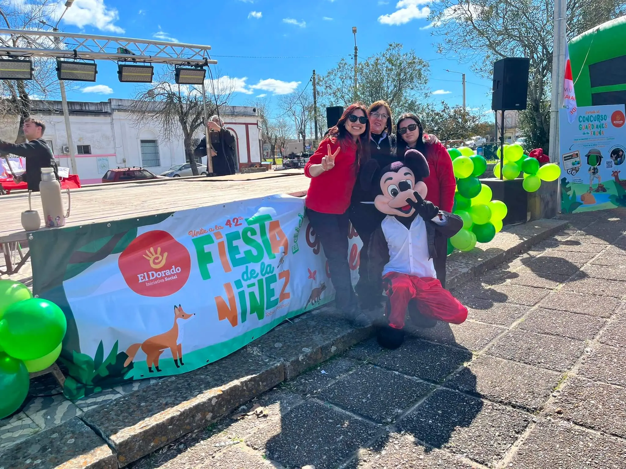 El equipo de El Dorado posa con Mickey junto al cartel de la Fiesta de la Niñez en la plaza.
