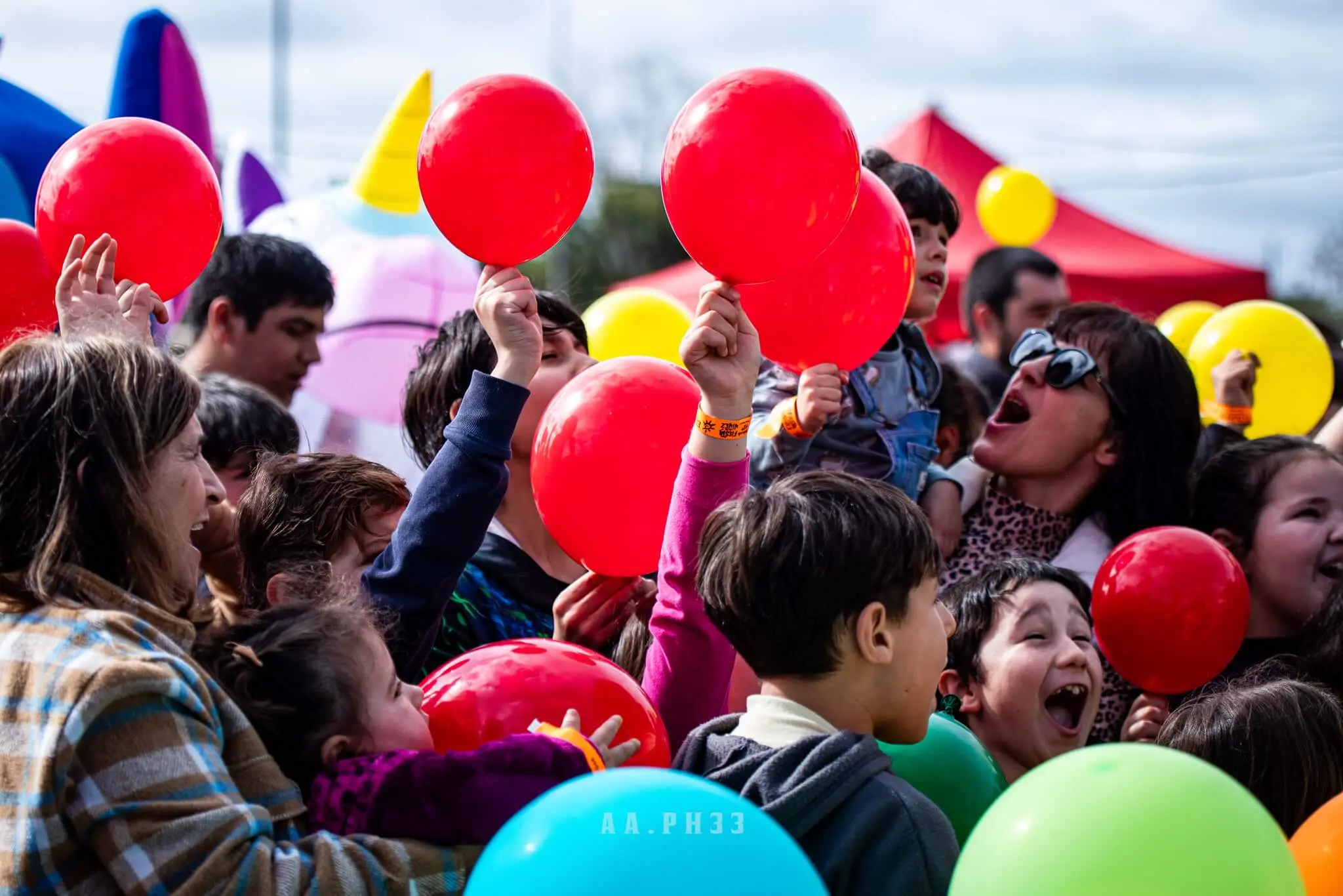 Niños festejan y estiran los brazos para atrapar globos rojos.