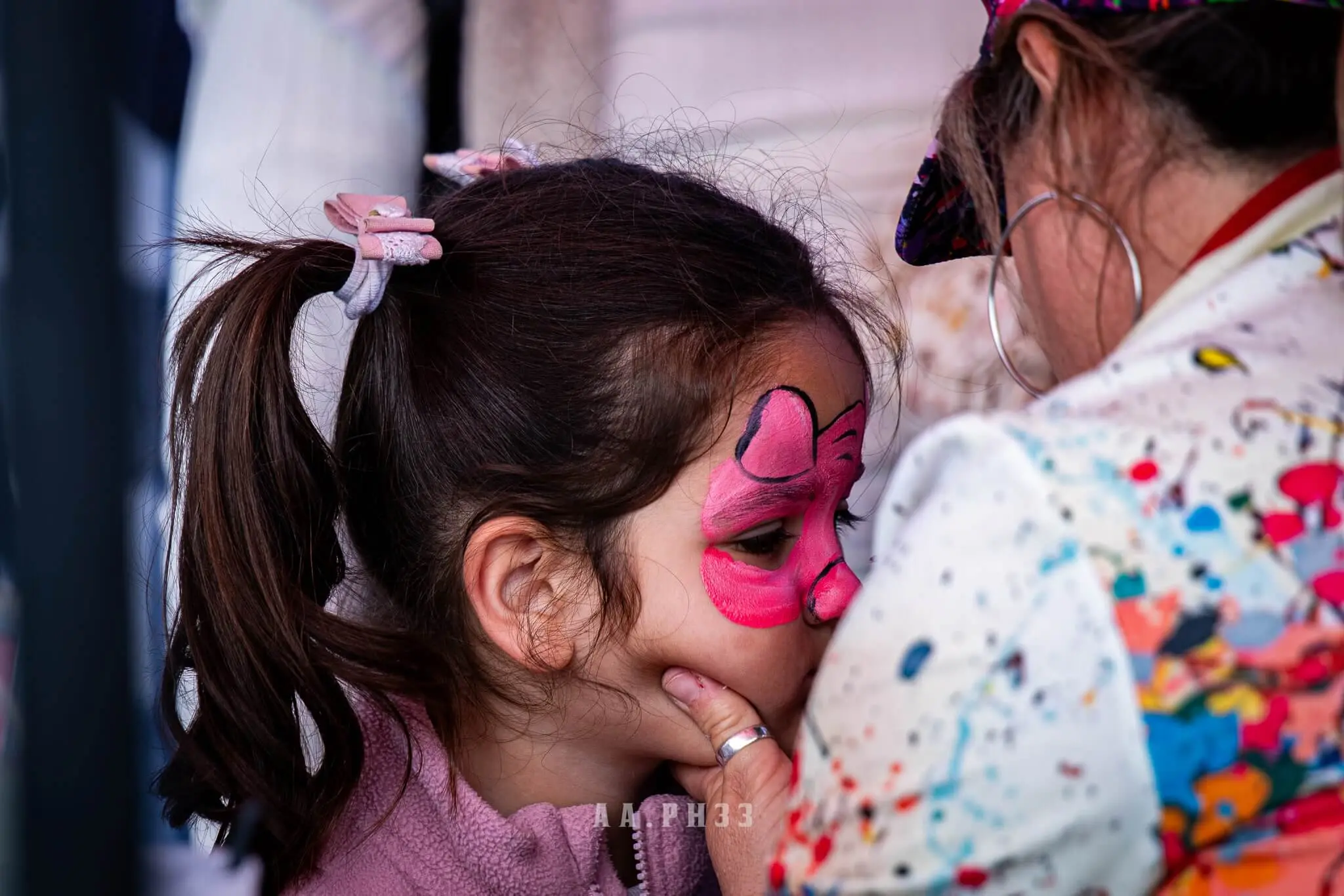 Una niña con la cara pintada de mariposa rosada abraza a una mujer.